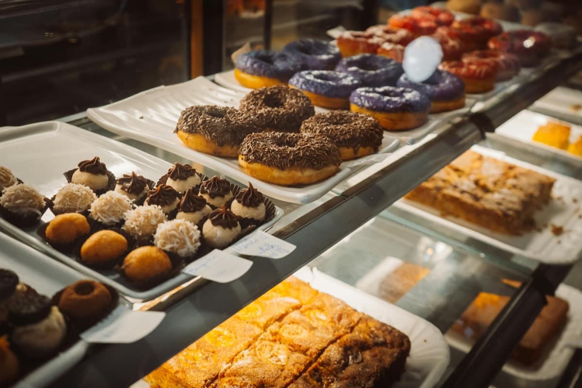 A bakery display case filled with trays of donuts and pastries (16:9)