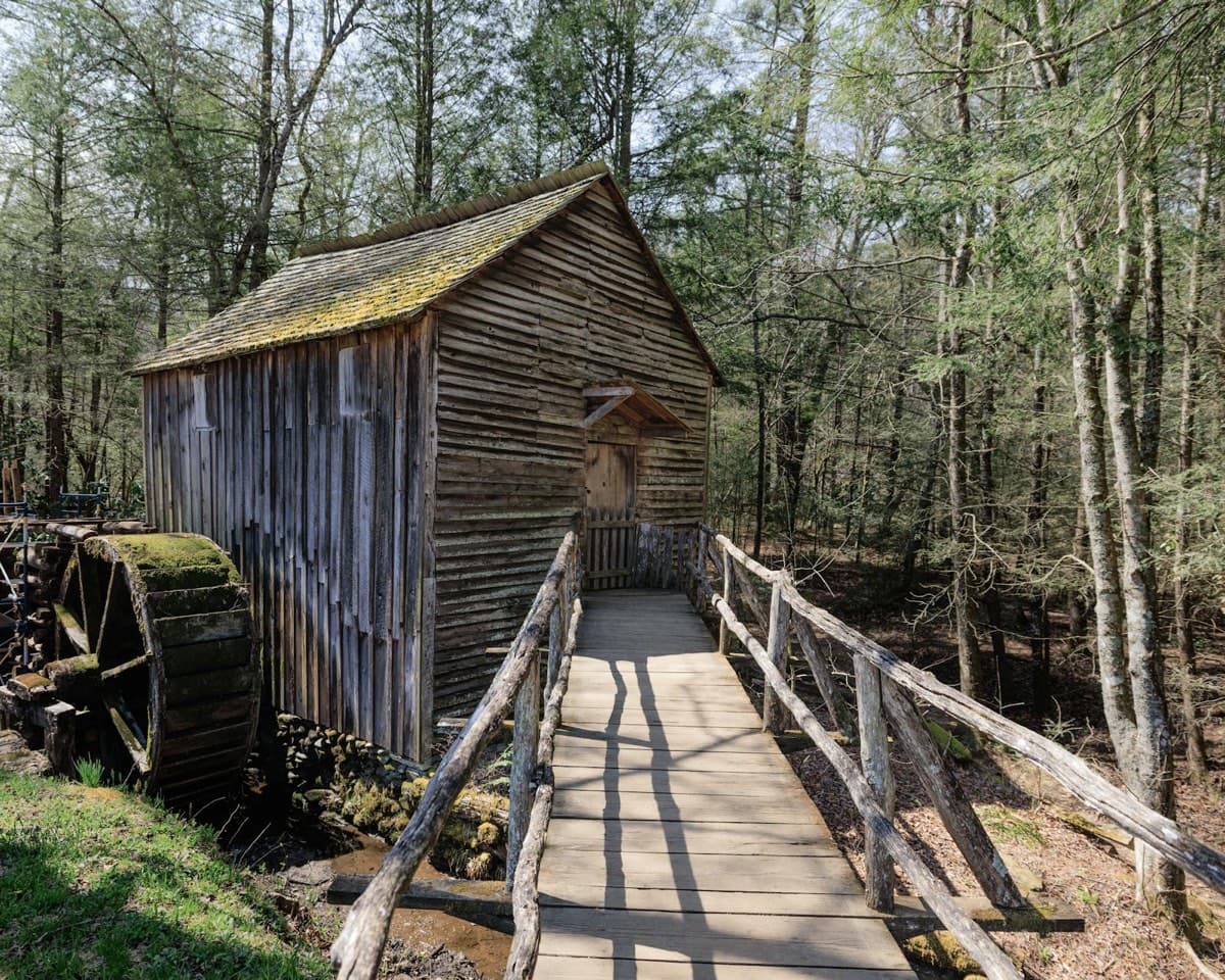 A historic wooden grist mill with a water wheel and footbridge in a Tennessee forest (16:9)