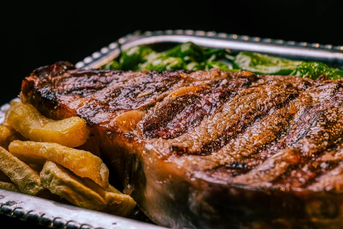 A thick char-grilled steak served with steak fries on a metal platter (16:9)