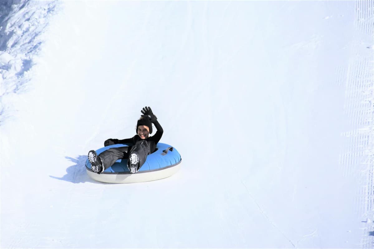 A child waving while sliding down a snowy slope in a blue snow tube (16:9)