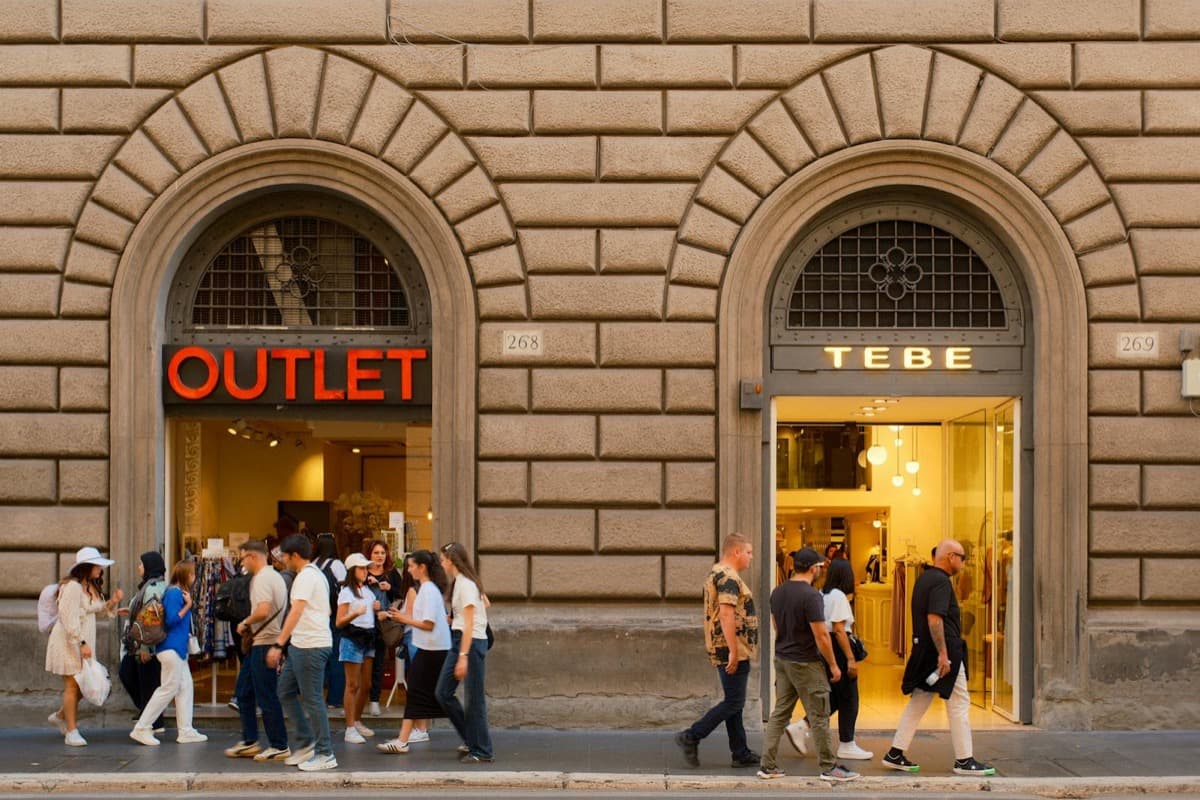Shoppers walking past outlet store storefronts along a street (16:9)