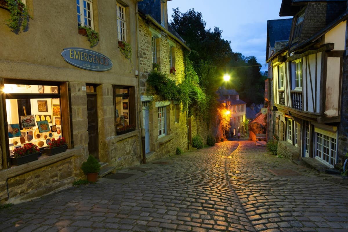 A lamplit cobblestone street lined with European-style stone shops at dusk (16:9)