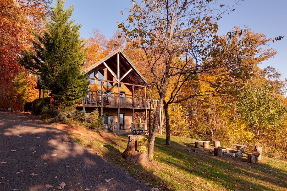 Thistle Britches cabin framed by autumn trees with its fire pit and Smoky Mountain setting