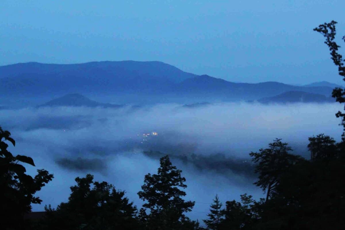 Early morning fog filling the valley below with mountain ridges and city lights peeking through the mist