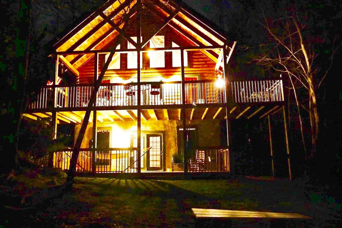 Cabin front view at night with warmly lit upper and lower wraparound decks