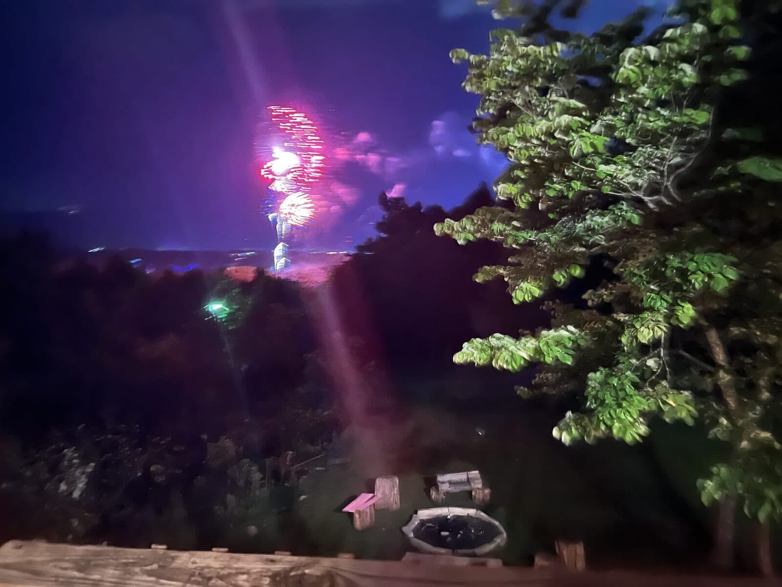 Pink fireworks bursting in the night sky above the Thistle Britches firepit and deck rail